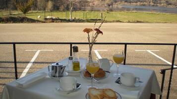 A table set with breakfast items including croissants, juice, and coffee, overlooking a scenic landscape with a lake and hills.