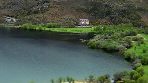 Una propiedad junto al lago con un edificio grande, rodeada de exuberante vegetación y colinas.
