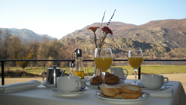 Una mesa lista para el desayuno con croissants, jugo y café, con vistas a un paisaje montañoso.
