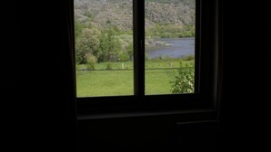 Vista desde una ventana de un paisaje montañoso con un lago, un campo cubierto de hierba y una cerca.