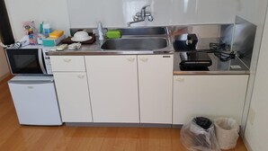Uma cozinha compacta com micro-ondas, geladeira, pia e um pequeno balcão com diversos objetos.