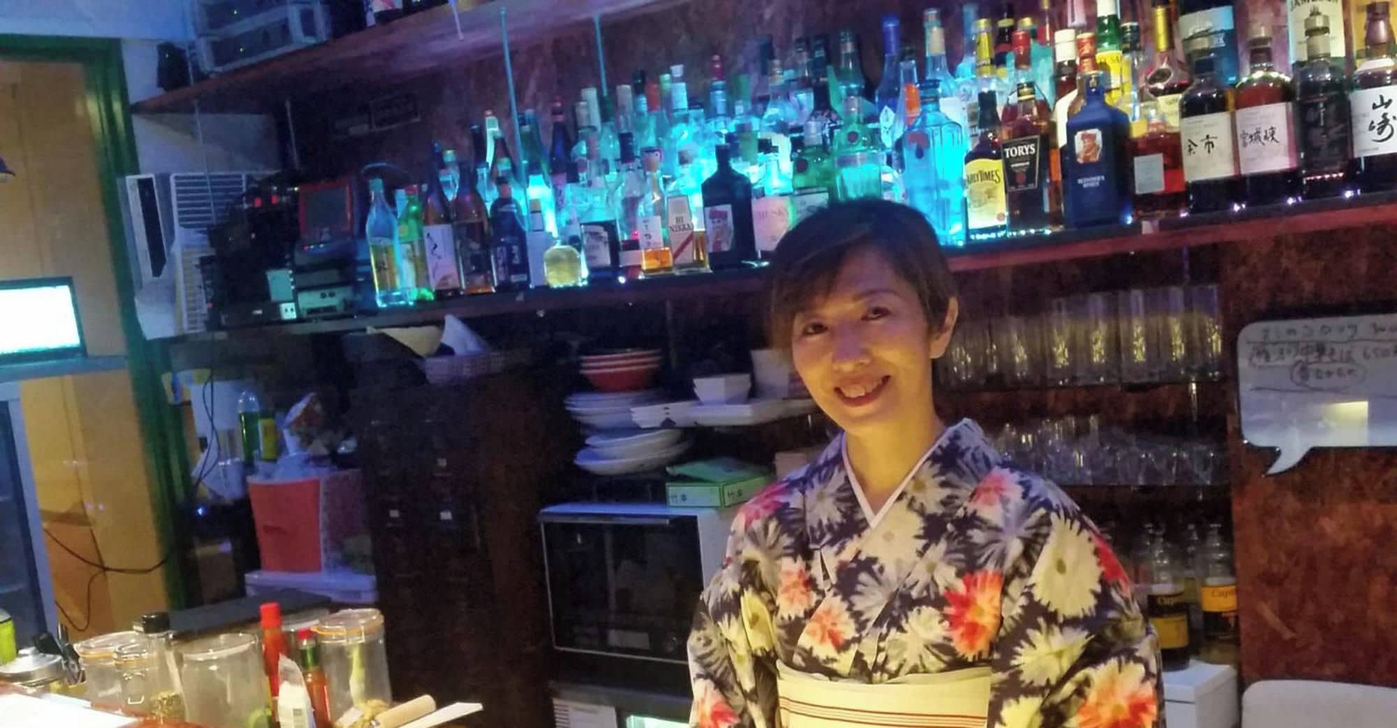 Una persona de pie frente a una barra con estantes llenos de varias botellas.