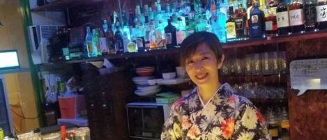 Una persona de pie frente a una barra con estantes llenos de varias botellas.