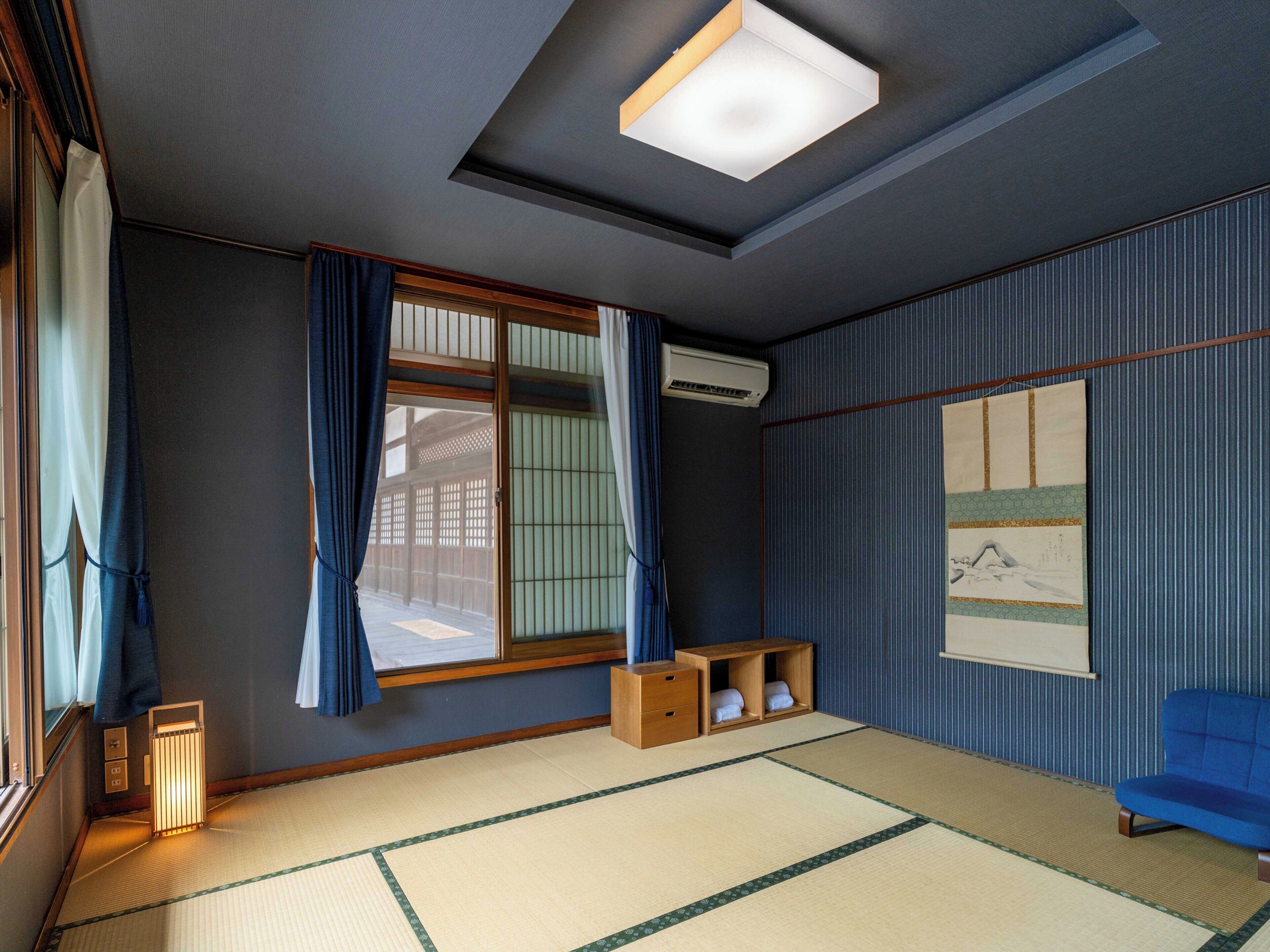 Ein traditioneller japanischer Raum mit Tatami-Boden, einer Schiebetür, einem blauen Sofa und einer Deckenleuchte.