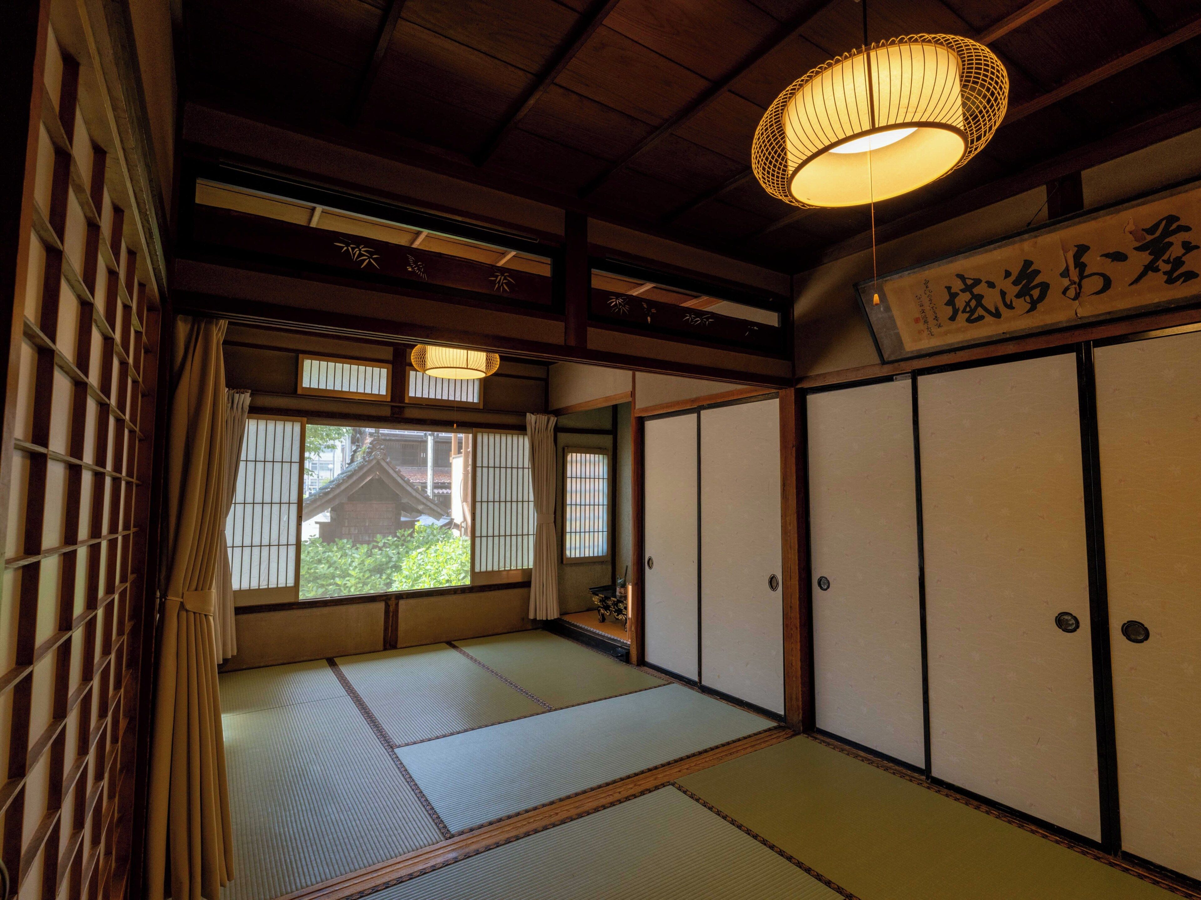 Een traditionele Japanse kamer met tatami vloerbedekking, schuifdeuren en een hanglamp.