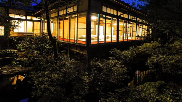 A traditional Japanese-style building with large windows and a wooden exterior, surrounded by dense foliage. - Temple Hotel Takayama Zenkoji (Takayama)
