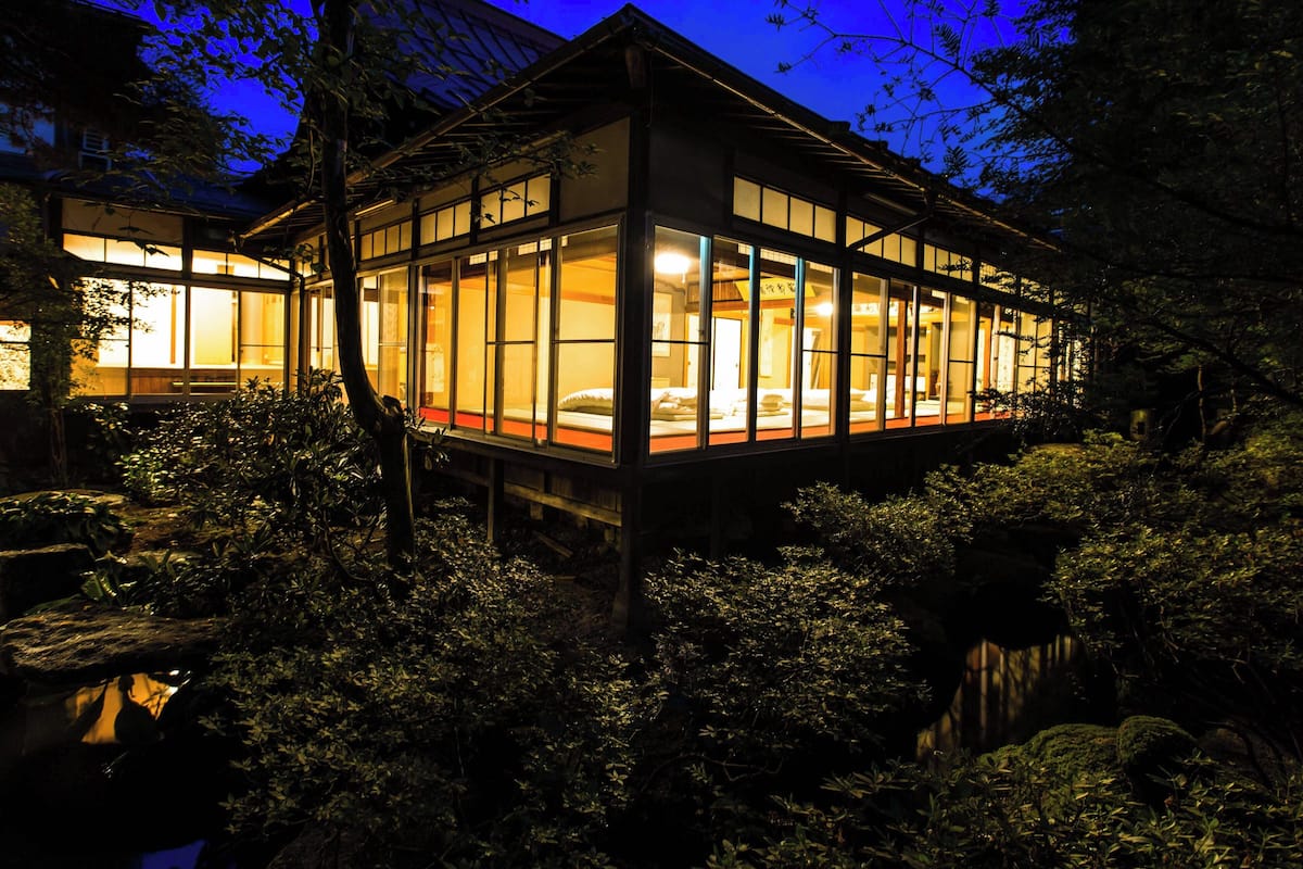 Un edificio tradicional japonés con amplios ventanales y fachada de madera, rodeado de abundante follaje.