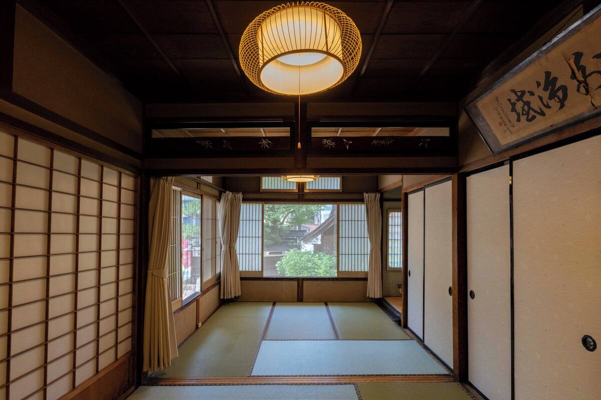 Una habitación japonesa tradicional con suelo de tatami, puertas correderas y una lámpara colgante.