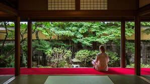 A traditional Japanese room with tatami flooring, a red carpet, and a view of a lush garden. - Temple Hotel Takayama Zenkoji (Takayama)