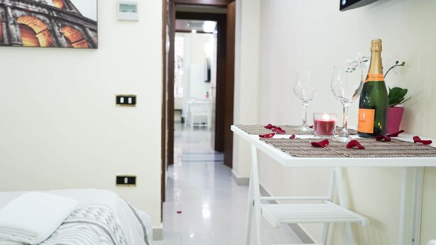 A hotel room with a bed, a table set with a bottle of champagne, glasses, and a candle. - Termini Guesthouse (Rome)