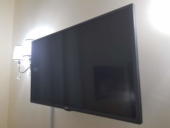 A flat-screen TV mounted on a wall with a light fixture to the left. - Termini Guesthouse (Rome)