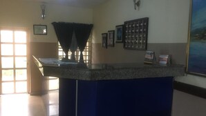 A reception area with a counter, a framed certificate on the wall, and a window with blinds. - Villa Savoye Hotels and Resorts (Lekki)