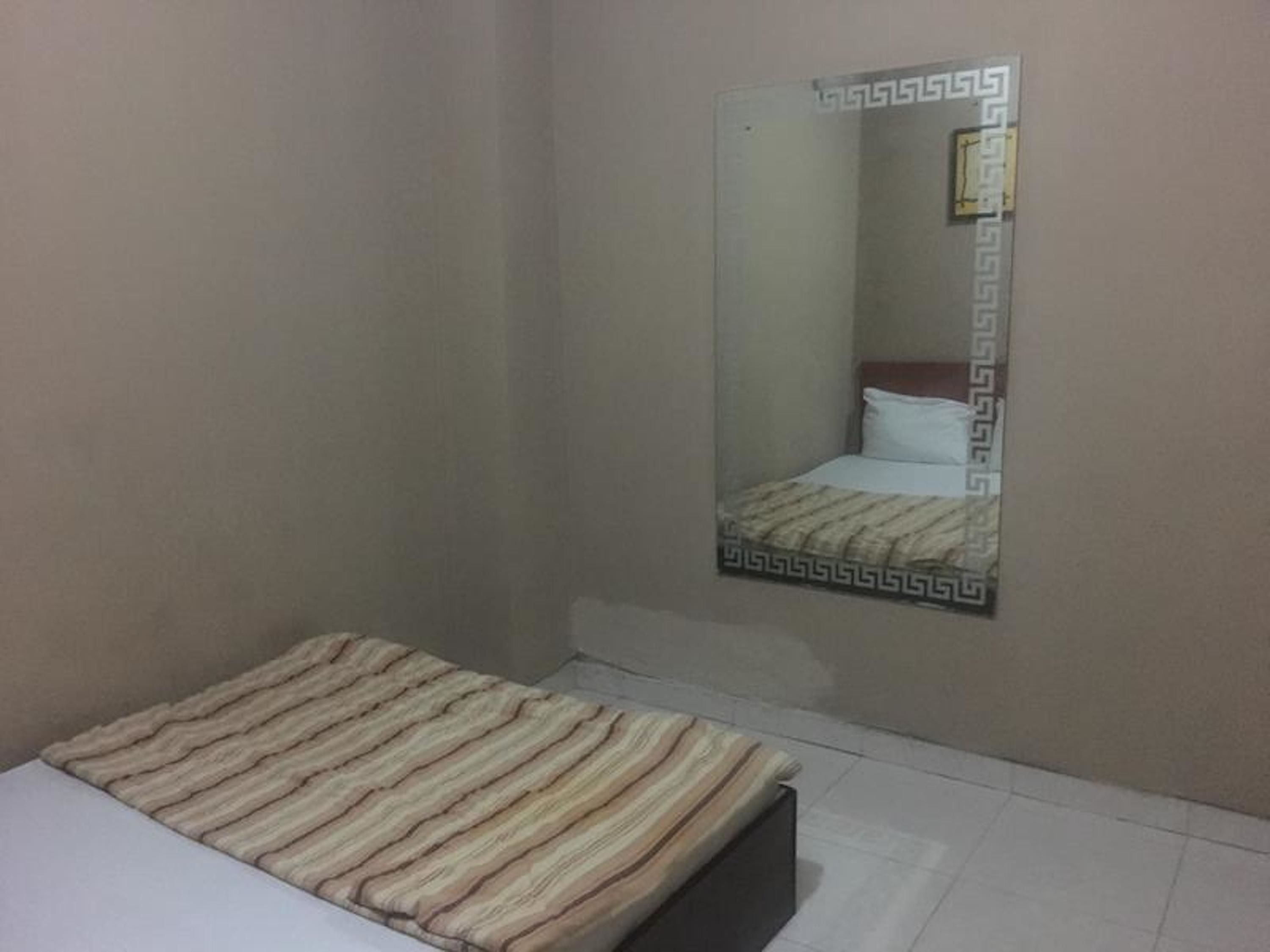 A small, single-bed room with a striped bedspread, a plain wall, and a mirror with a decorative frame.