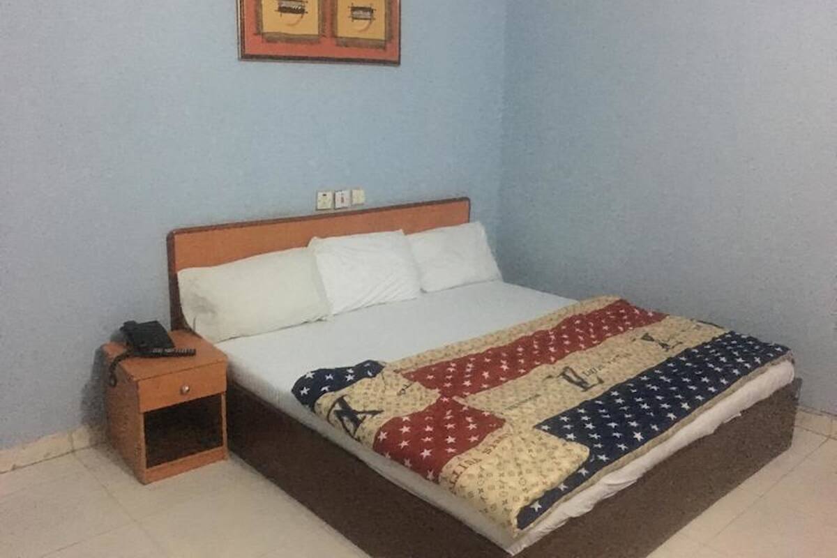 A single bed with a quilted blanket, a wooden nightstand, and a framed picture above the bed.