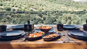 Une table à manger dressée avec des assiettes, des bols et des couverts, donnant sur un paysage montagneux.