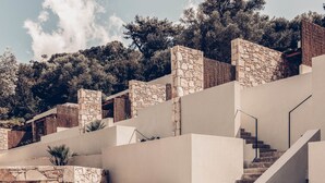 Un bâtiment moderne avec une façade en pierre, un escalier et une vue sur les arbres en arrière-plan.