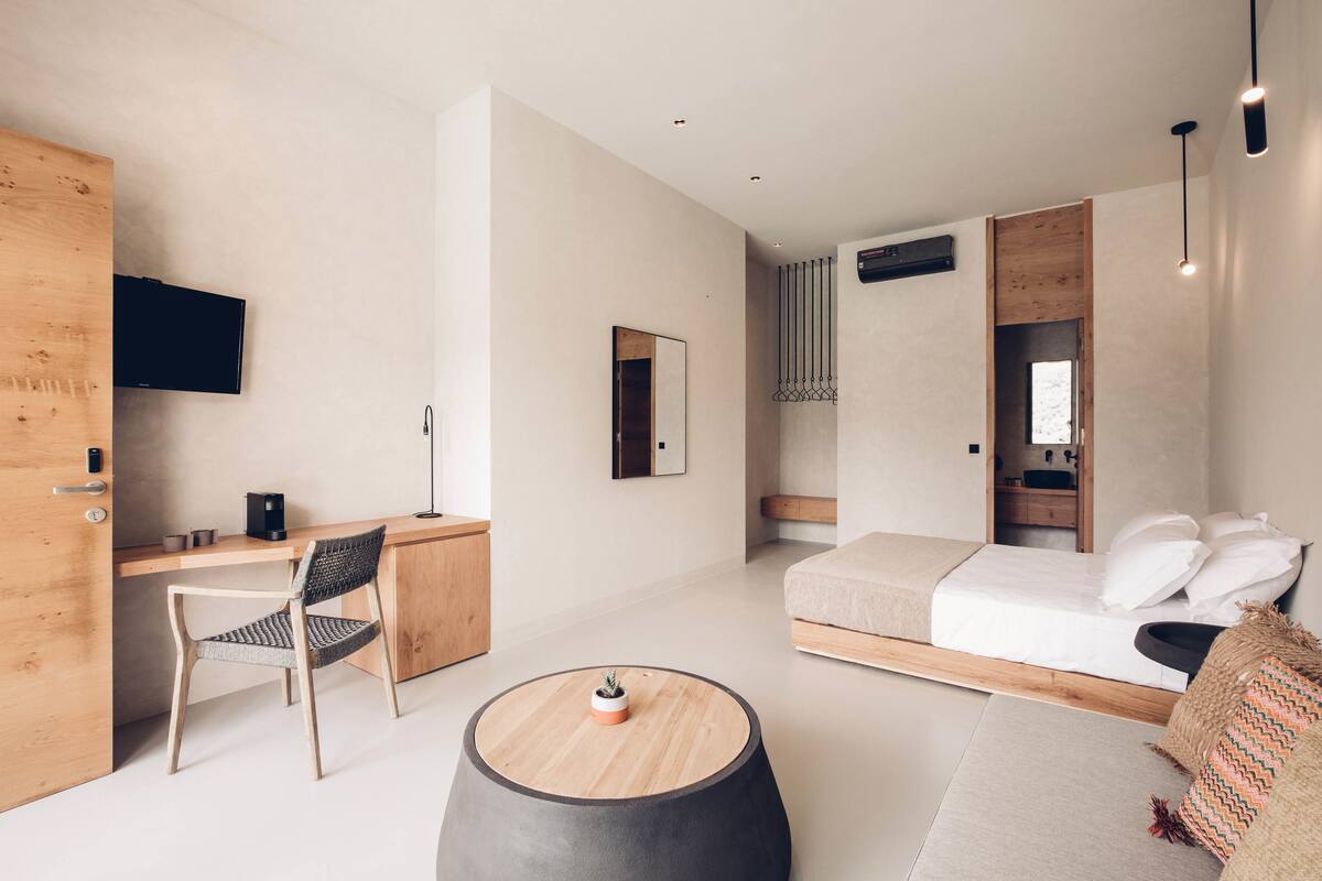 Una habitación de hotel moderna con un escritorio de madera, una cama individual, una mesa redonda de centro y un televisor instalado en la pared.