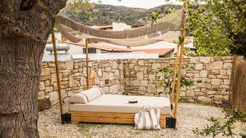 A hammock bed setup with a stone wall backdrop, a tree, and a view of buildings in the background.