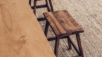 A wooden table and two stools in a room with a concrete floor and a woven rug.