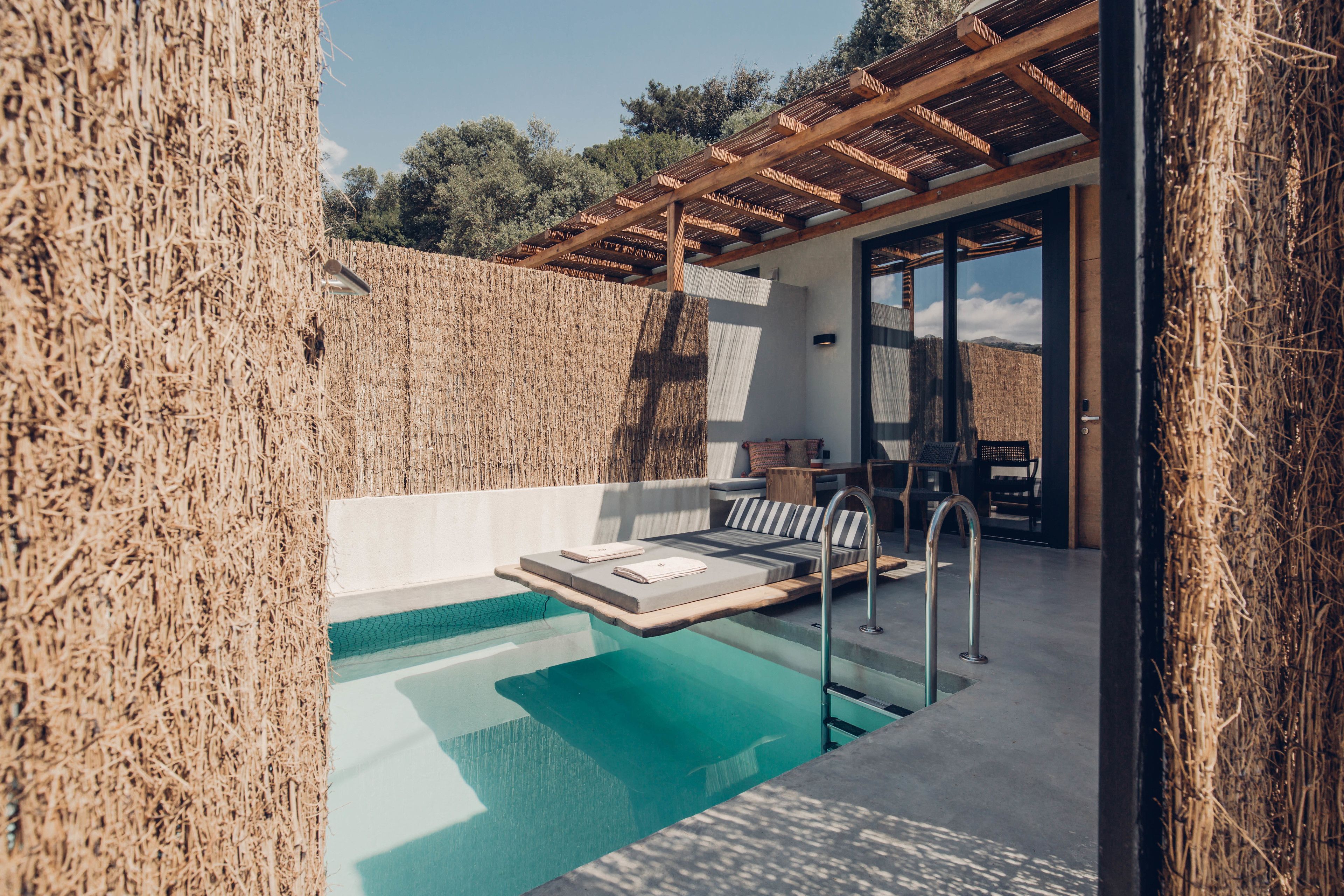 Un área de piscina moderna al aire libre con un pérgola de madera, zona de estar con cojines y vistas del paisaje circundante.
