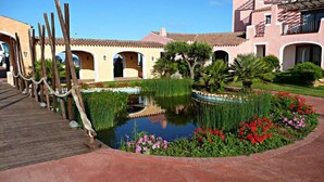 A courtyard with a central pond, surrounded by a wooden deck and a variety of plants and flowers. - Stintino Country Paradise (Stintino)