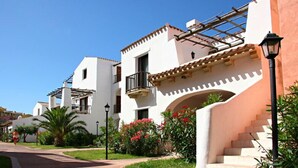A residential building with a white facade, multiple balconies, and a garden area with red flowers. - Stintino Country Paradise (Stintino)