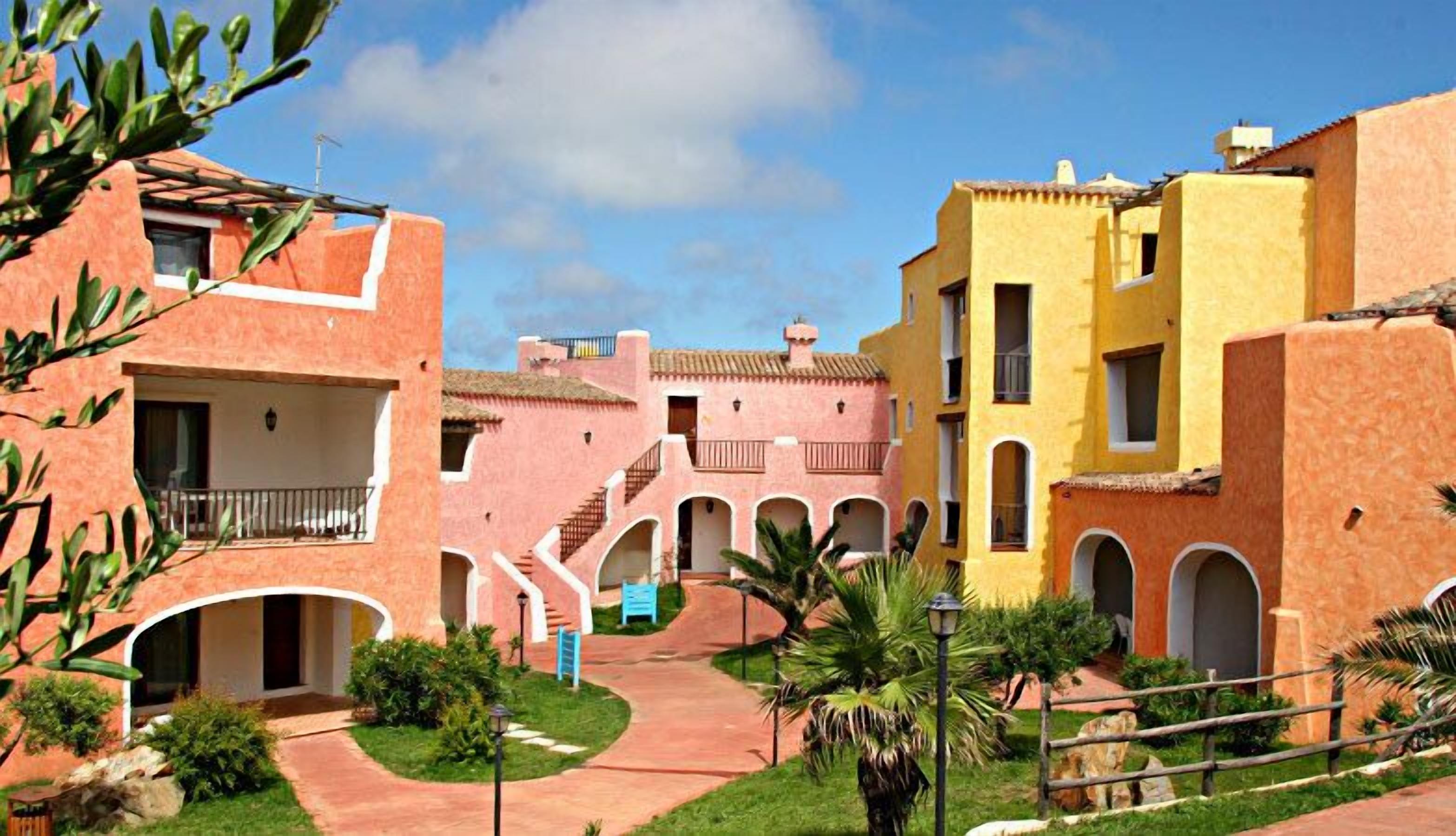 Un patio con edificios que tienen ventanas arqueadas y balcones, rodeado de vegetación y un cielo despejado.