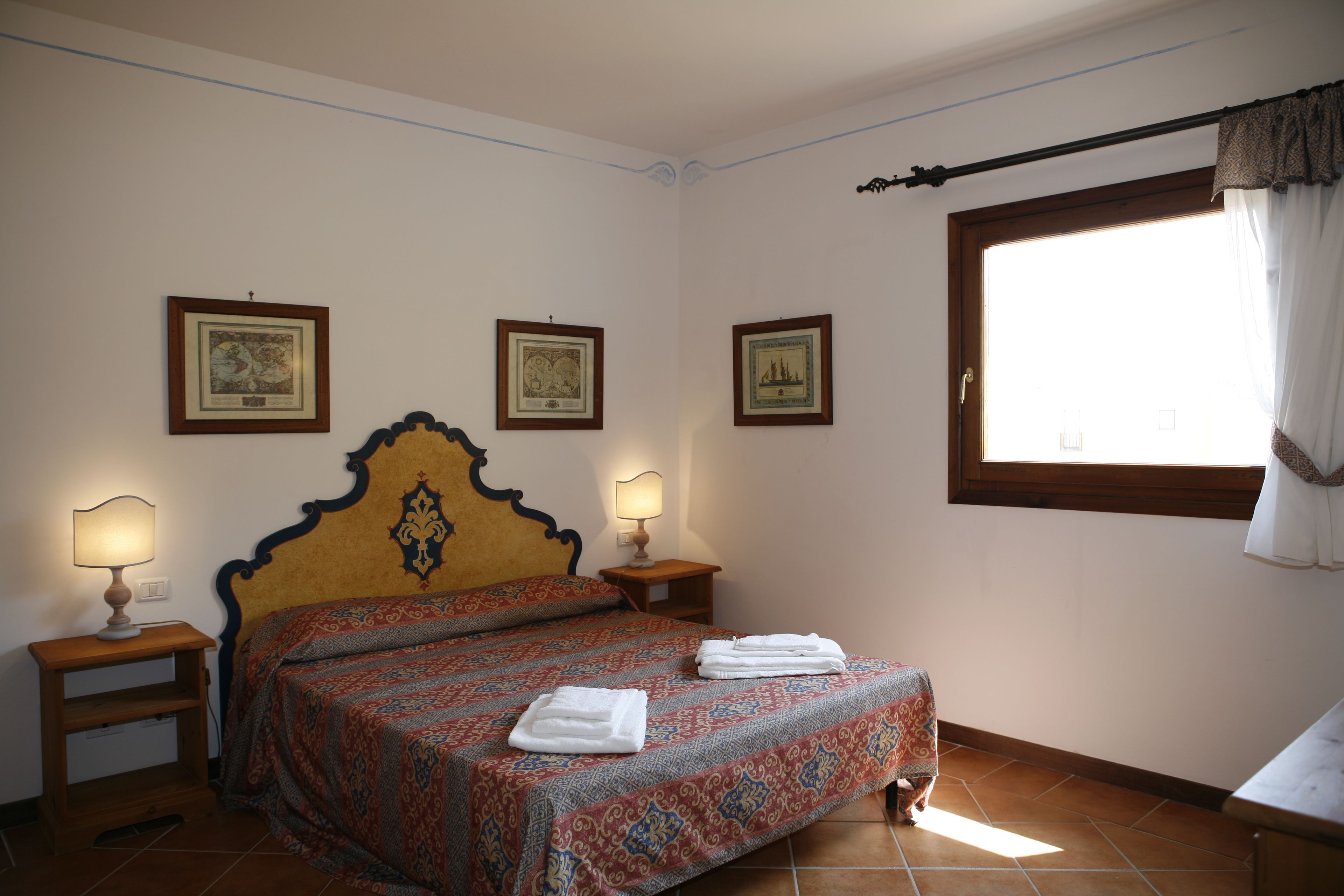A bedroom with a large bed, two bedside tables with lamps, and three framed pictures on the wall.