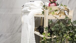 Una estantería de madera con toallas blancas y una planta en maceta en un baño con baldosas de mármol.