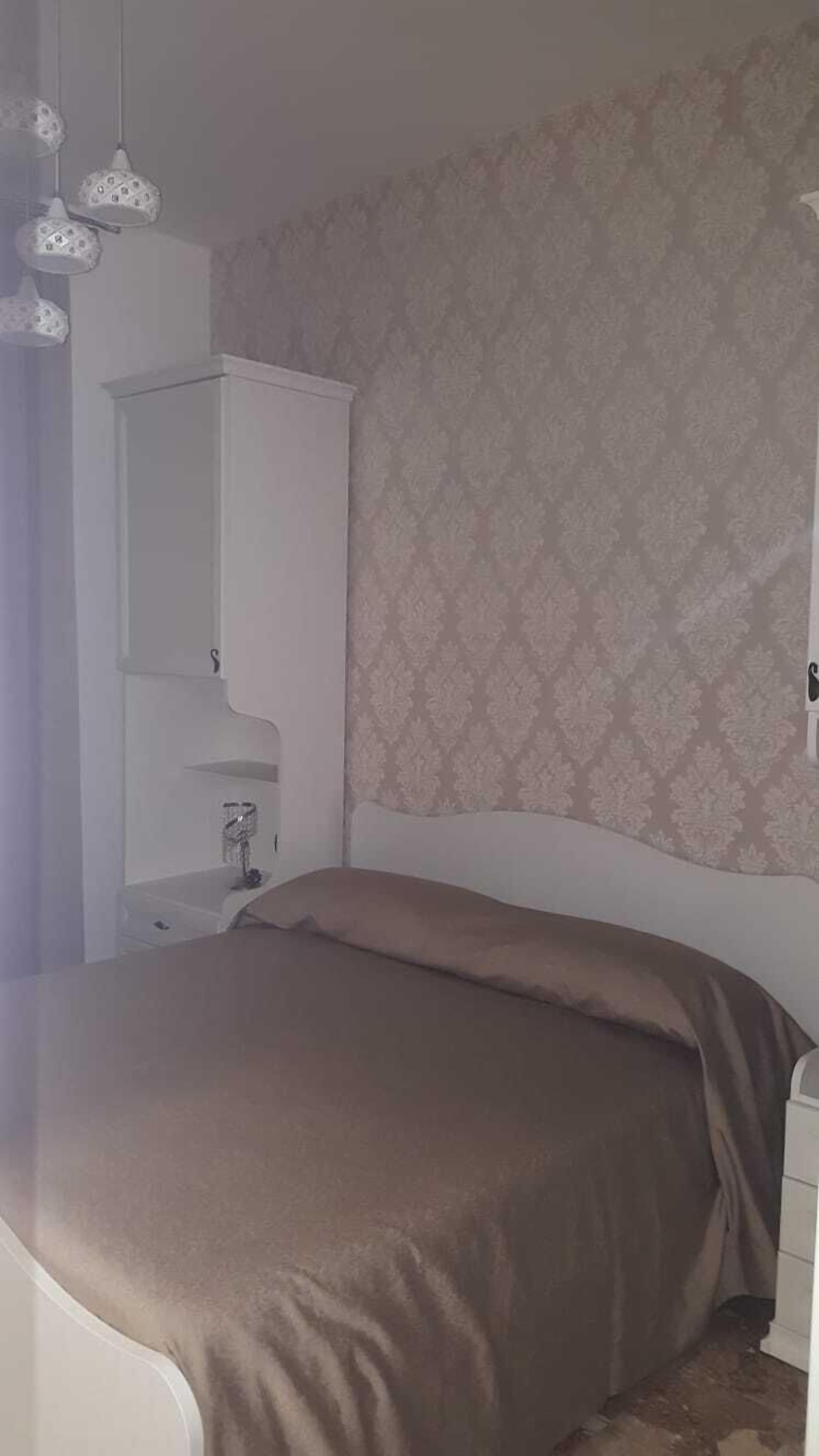 A bedroom with a bed, a nightstand, a dresser, and patterned wallpaper.