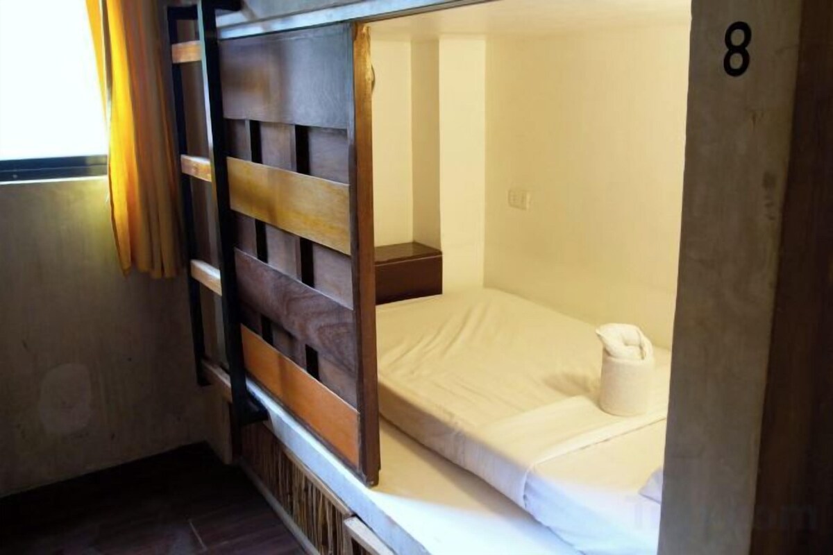 A bunk bed with a wooden headboard, a small bedside table, and a number '8' on the wall.
