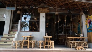A rustic outdoor seating area with wooden tables and chairs, a dog resting on the ground, and a sign reading "HAPPINES". - Happiness Hostel El Nido (El Nido)