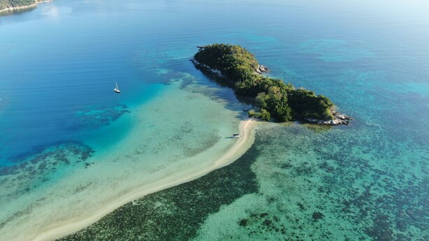 An aerial view of a tropical island with clear turquoise waters, a sandy beach, and dense green vegetation. - Happiness Hostel El Nido (El Nido)