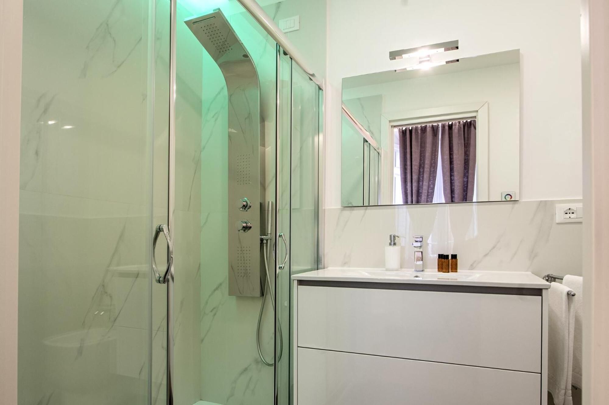 Um banheiro moderno com chuveiro em box de vidro, um lavatório branco com espelho e um porta-toalhas.