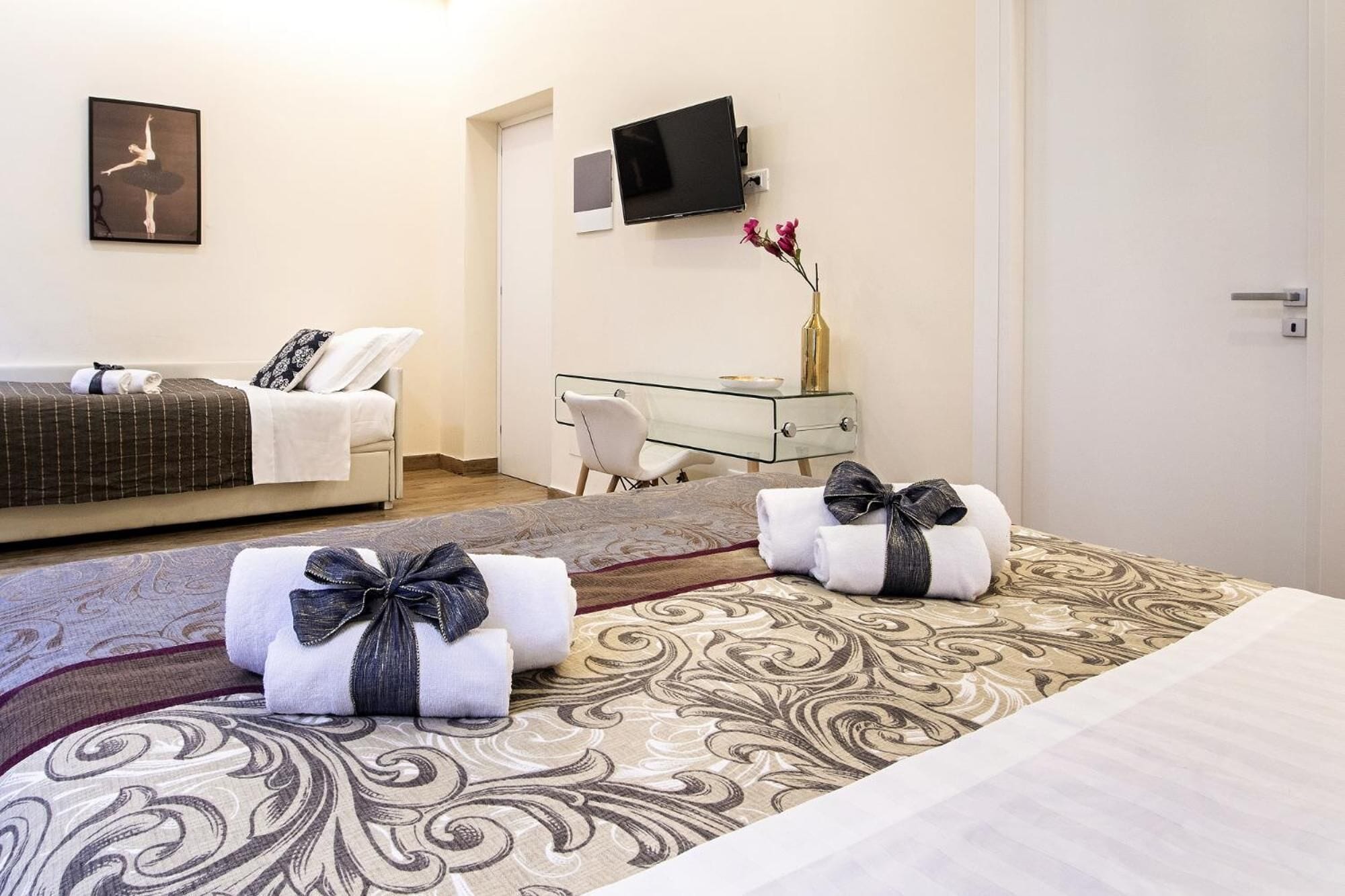 Une chambre d’hôtel avec un lit, un bureau, une chaise, une télévision et un vase avec des fleurs.