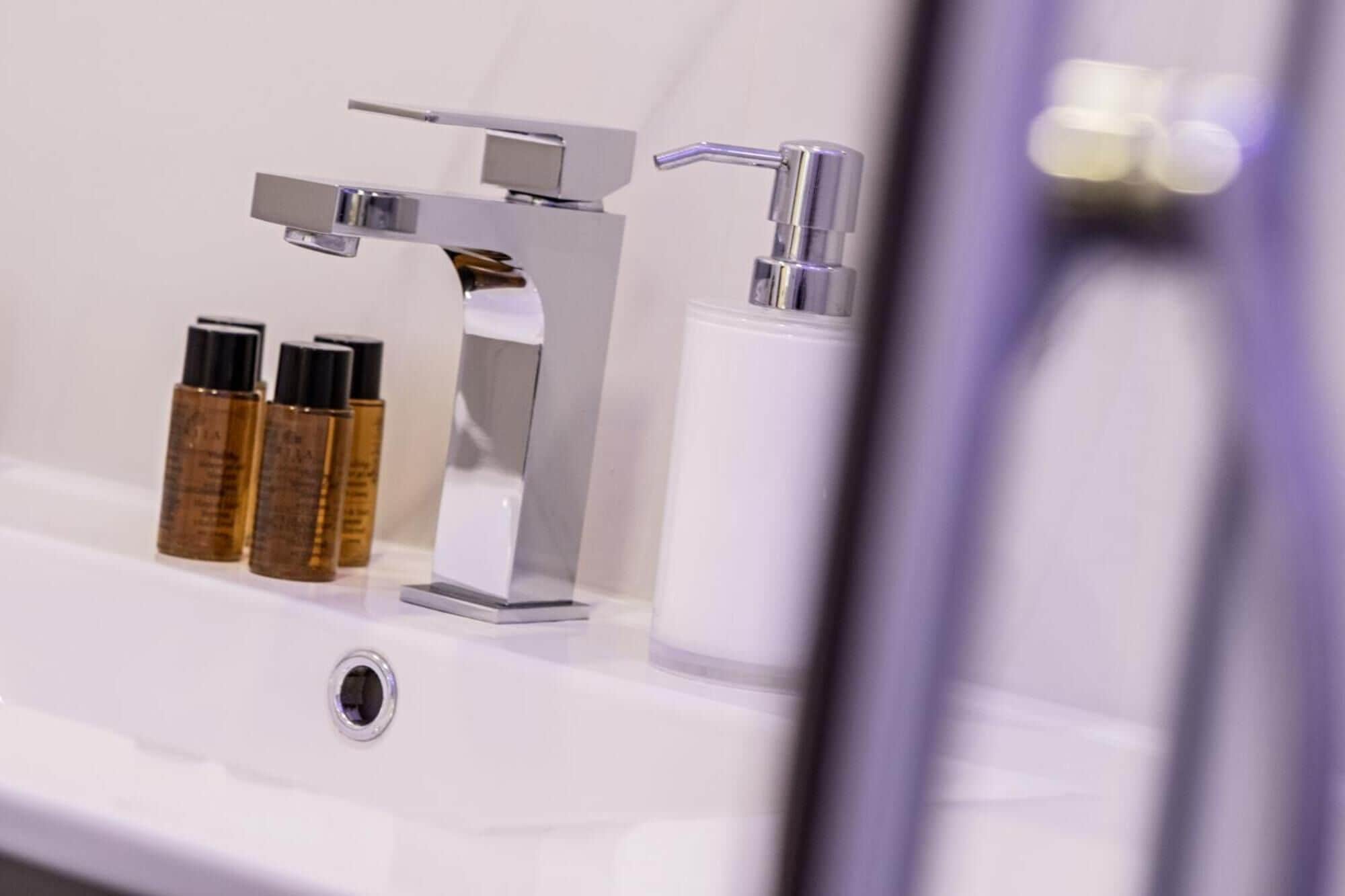 A bathroom sink with a chrome faucet, three bottles of toiletries, and a white soap dispenser.