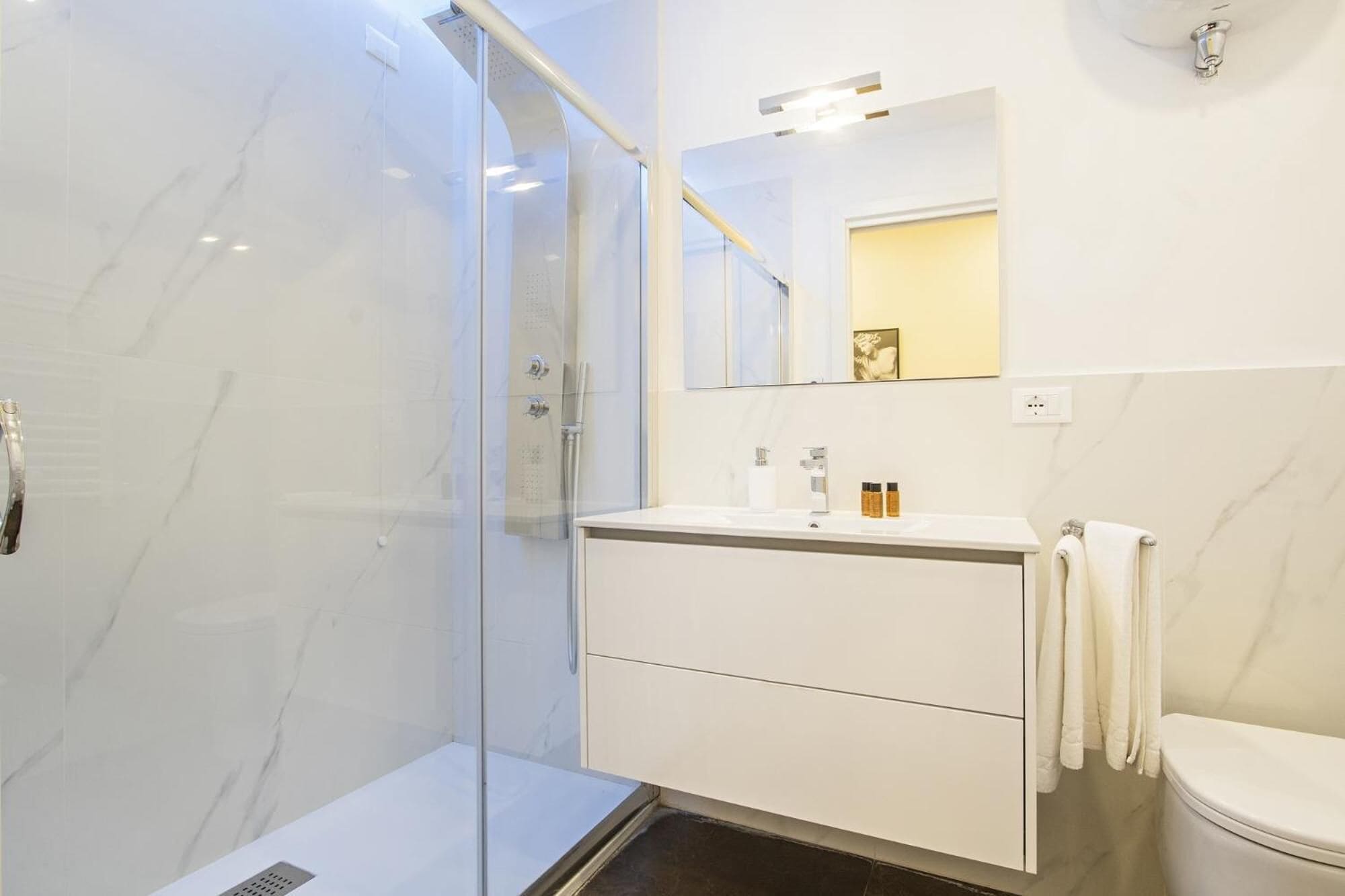Un baño moderno con cabina de ducha de vidrio, tocador blanco con espejo y un inodoro.
