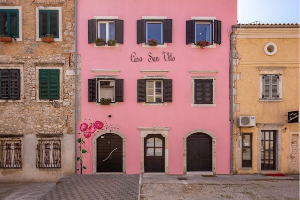 A pink building with the sign "Casa San Vito" and multiple windows with shutters.