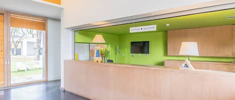 A reception area with a green wall, a reception desk, a TV, and a sign that reads 'RECEPCÃO' (Reception).