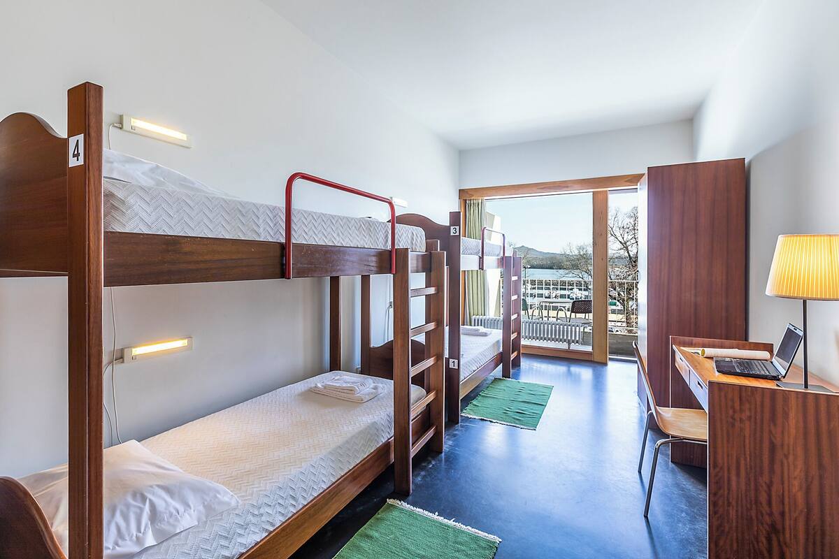 A bunk bed room with a desk and a laptop, a view of the outside, and a window.
