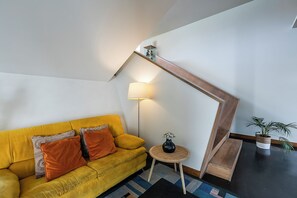 Una sala de estar moderna con un sofá amarillo, una lámpara, una mesita con un florero y una escalera.