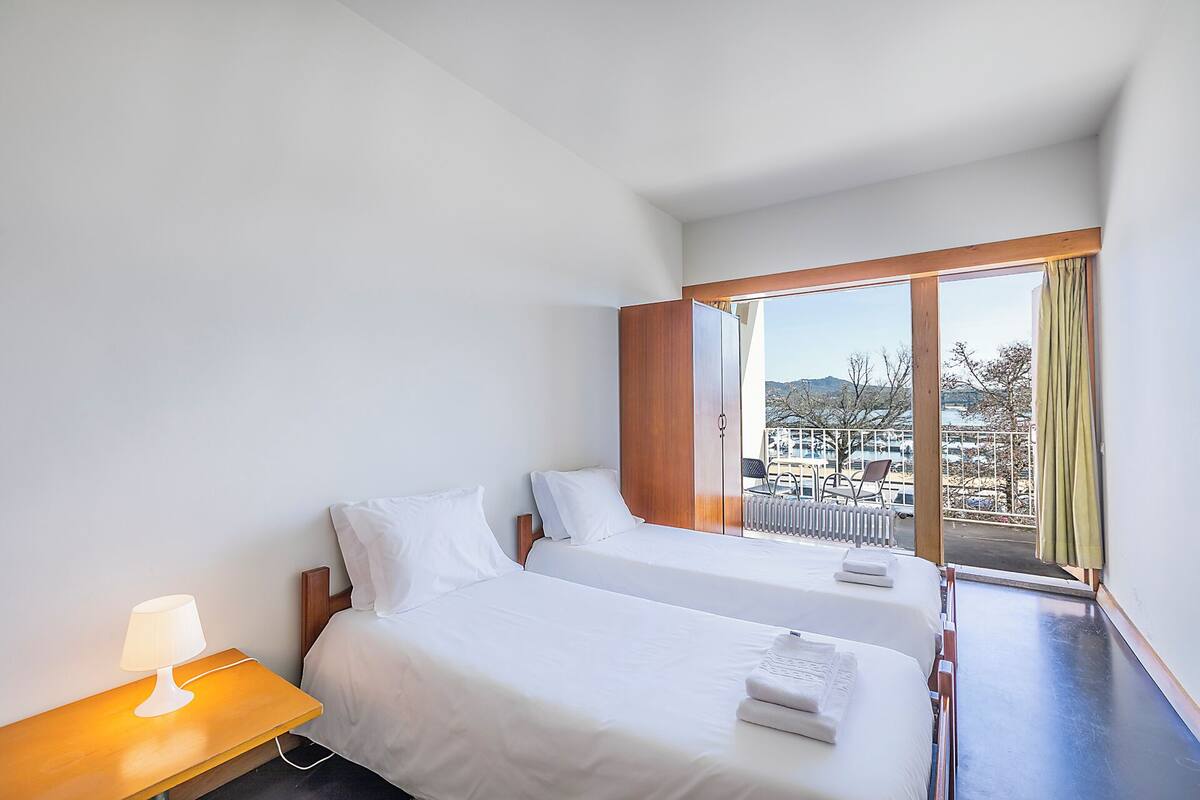A hotel room with two beds, a window with a view, a wooden nightstand, and a lamp.