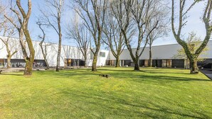 A modern building with a flat roof and large windows, surrounded by a well-maintained grassy area with trees. - HI Viana Castelo - Pousada de Juventude - Hostel (Viana do Castelo)