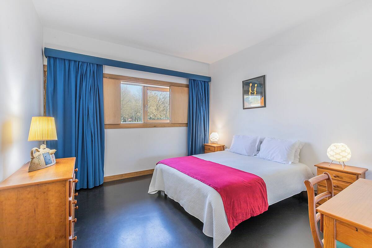 A bedroom with a bed, bedside tables, a lamp, a window with curtains, and a picture on the wall.