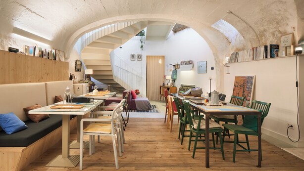 A cozy interior with a wooden dining table, chairs, a sofa, and a staircase leading to an upper level.