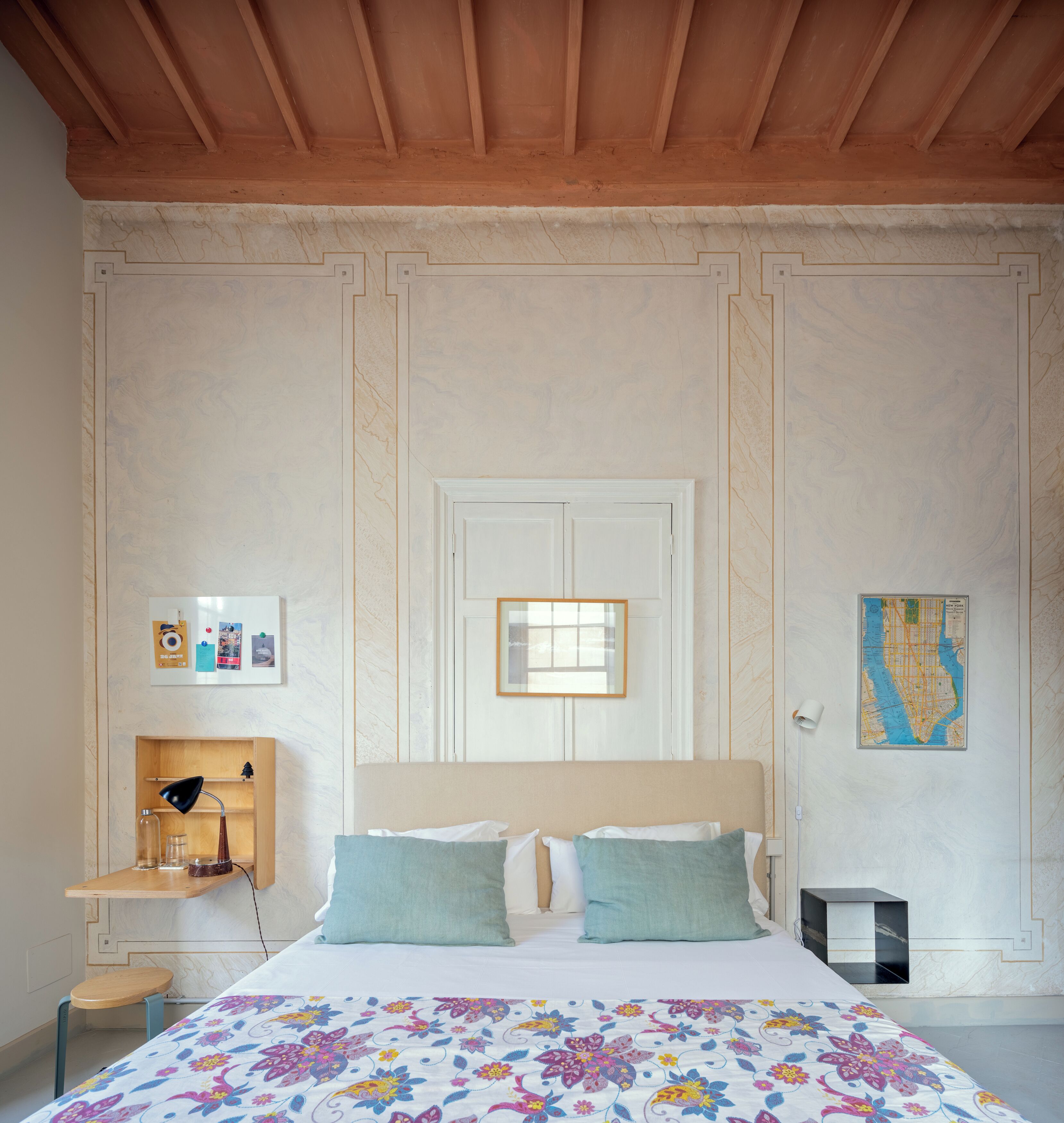 Un dormitorio con cama, mesita de noche, escritorio, silla, un mapa en la pared y una puerta.