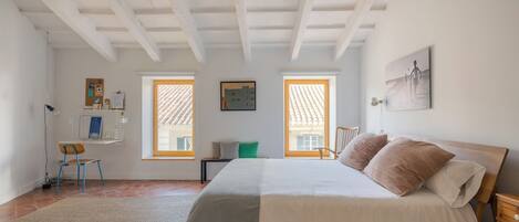 Un dormitorio con cama, escritorio, silla y dos ventanas.