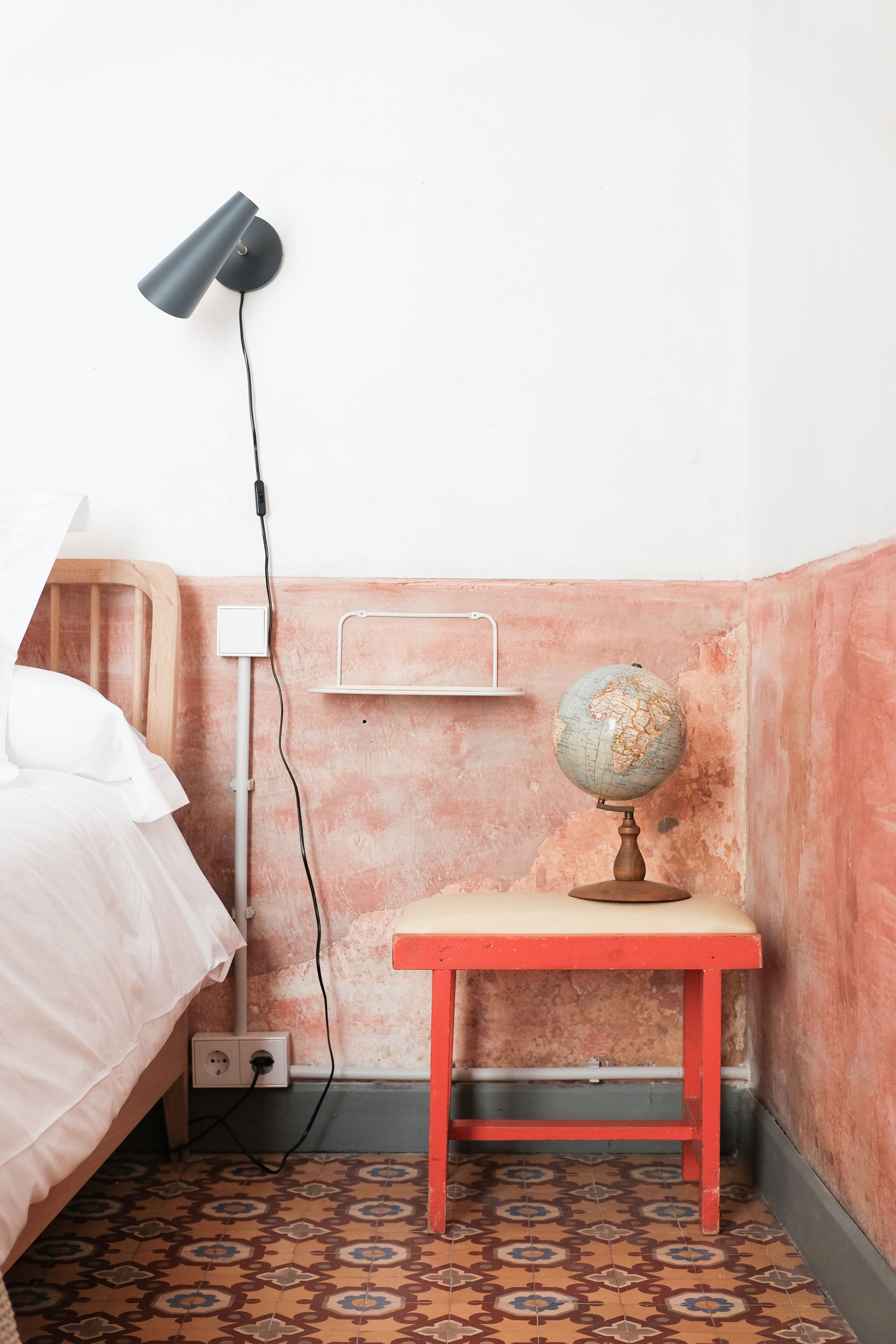 A small, compact room with a bed, a desk with a globe, a lamp, and a power outlet.
