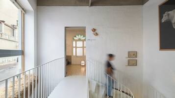 Un interior moderno con una escalera central, paredes blancas y vista a la calle.