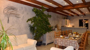 Uma sala de jantar com uma mesa posta para quatro pessoas, um vaso grande com planta e um sofá branco.